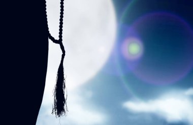 Müslüman bir kadının silueti ellerinde dua boncuklarıyla dua ediyor.