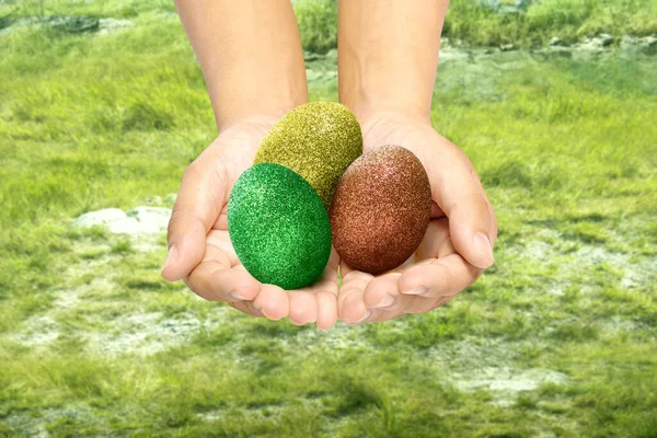 Human hands holding colorful easter eggs with meadow field background. Happy Easter