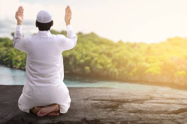 Asyalı Müslüman adamın el ele tutuşup dışarıda dua edişinin arkası.