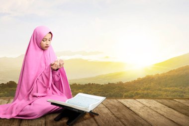 Duvak takmış Asyalı Müslüman kadın ellerini kaldırmış ve ahşap zeminde dua ediyor.