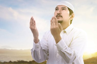 Asyalı Müslüman adam elini kaldırdı ve mavi gökyüzü arka planıyla dua etti.