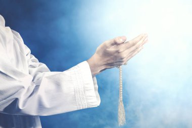 Müslüman bir adam ellerinde dua boncuklarıyla renkli bir geçmişle dua ediyor.