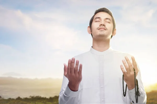 Asian Muslim man praying with prayer beads on his hands with blue sky background