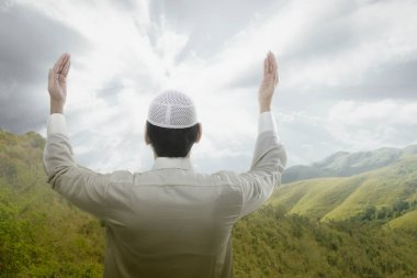 Asyalı Müslüman adamın dikiz aynasından el kaldırması ve dramatik bir arka planla dua etmesi.