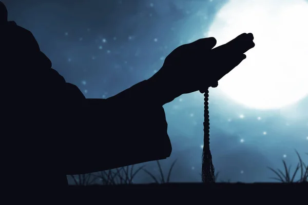 Silhouette of Muslim man praying with prayer beads on his hands with a night scene background