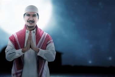 Asyalı Müslüman adam karşılama jesti ile ayakta duruyor.