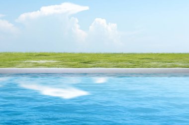 Gölette mavi su, yeşil çimenler ve mavi bir arka plan.