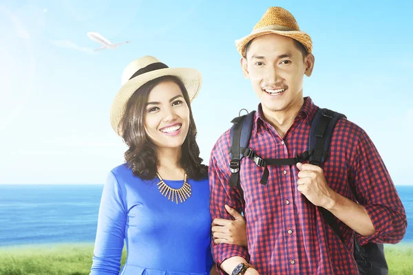 带着帽子和背包的亚洲夫妇带着海景在球场上旅行 — 图库照片