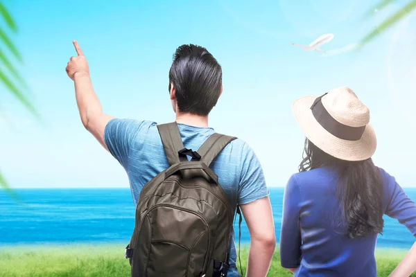 Rear view of Asian couple with hat and backpack looking at ocean view with a blue sky background