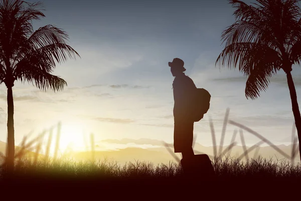 バックパックとスーツケースを背景に夕焼け空のフィールドに立っている男のシルエット — ストック写真