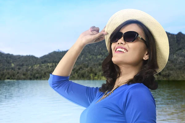 丘と青空の背景を持つ湖の上に帽子とサングラスを持つアジアの女性 — ストック写真
