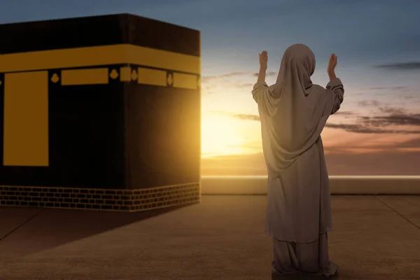 アジア系ムスリムの少女をベールに身を包み 日没シーンを背景にカアバの前で手を挙げ — ストック写真