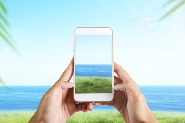 İnsan eli cep telefonuyla sahada deniz manzaralı bir fotoğraf çekiyor.