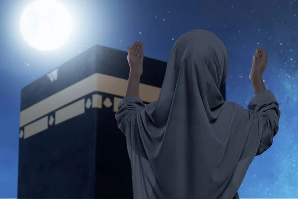アジア系ムスリムの少女をベールに身を包み 夜景を背景にカアバの前で手を挙げ — ストック写真