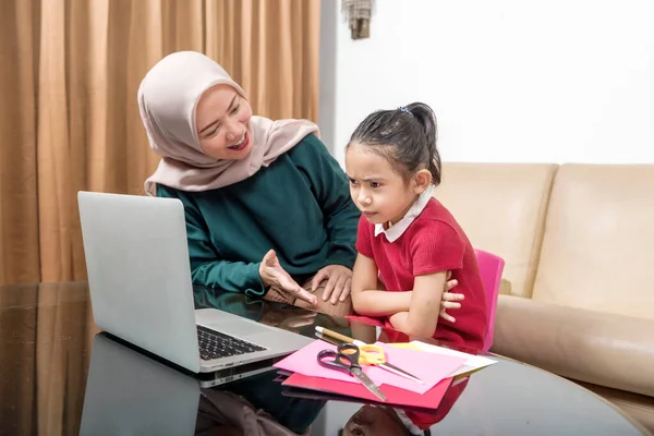 Asian mother helping little girl doing her homework with laptop at home. Online education during quarantine