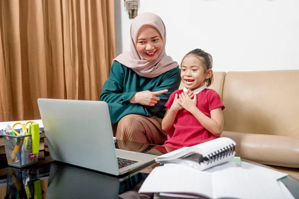 アジアの母親は女の子が家でノートパソコンで宿題をするのを手伝っている 隔離中のオンライン教育 — ストック写真
