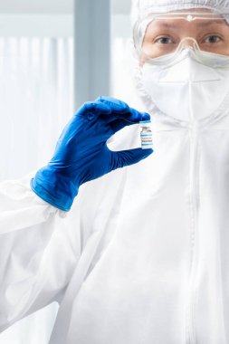 Koruyucu giysili ve eldivenli bir sağlık çalışanı hastanedeki 19 aşıyı elinde tutuyor.