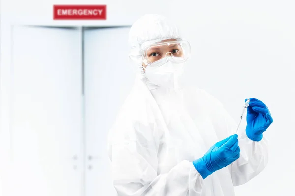 保護スーツと手袋を持っている健康労働者の女性病院でCovid 19ワクチンを保持 — ストック写真
