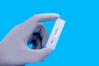 Koruyucu eldivenli bir sağlık çalışanı elinde renkli arkaplanlı kovid 19 antijen test kiti tutuyor.