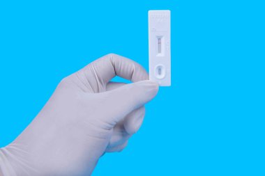 Koruyucu eldivenli bir sağlık çalışanı elinde renkli arkaplanlı kovid 19 antijen test kiti tutuyor.