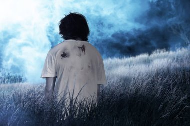 Vücudunda kan ve yara olan korkunç bir zombi sahada yürüyor.