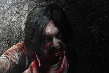 Vücudunda kan ve yara olan korkunç zombi grunge duvar arka planıyla sürünüyor.