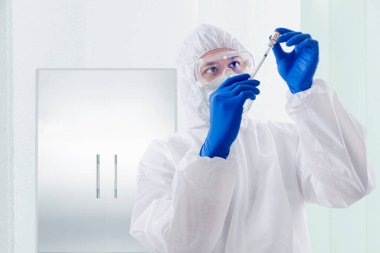 Koruyucu giysili ve eldivenli bir sağlık çalışanı hastanedeki 19 aşıyı elinde tutuyor.