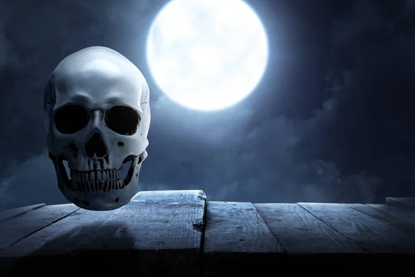夜の風景を背景に木製のテーブルの上に人間の頭蓋骨 — ストック写真