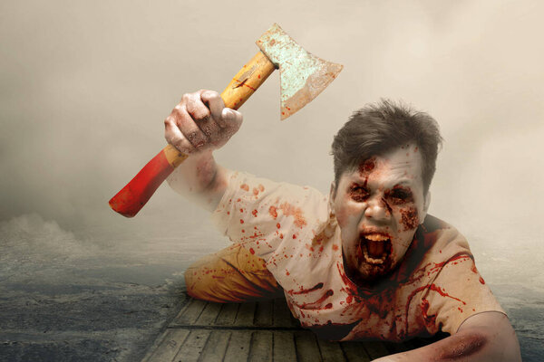 Scary zombie with blood and wound on his body holding ax crawling with foggy background