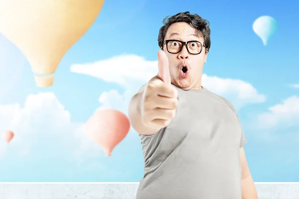 青い空を背景に飛んでカラフルな空気風船で親指を示す眼鏡を持つアジアの男 — ストック写真