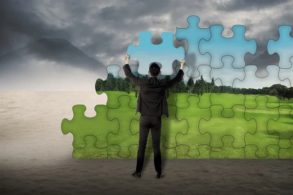 Geschäftsmann setzt Puzzle zusammen, um von Wüste zu Landschaft zu wechseln lizenzfreie Stockbilder