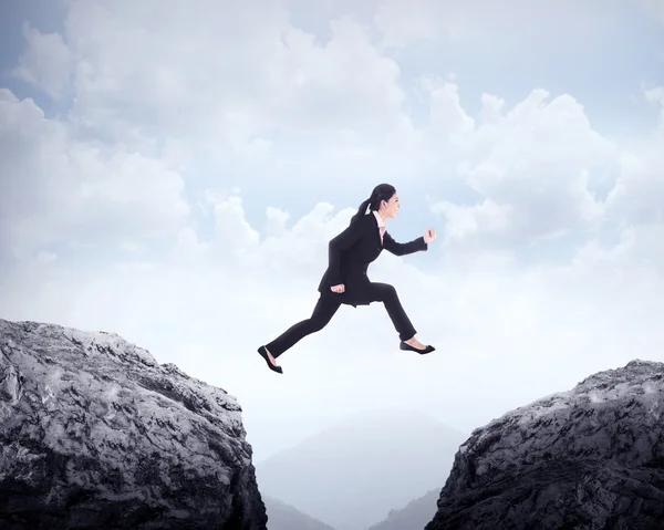 Business woman jumping across hill — Stock Photo, Image