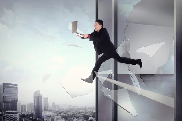 Hombre con portátil saltar a través de la ventana del edificio de oficinas — Foto de Stock