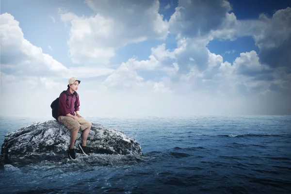 Молодой азиатский путешественник сидит на скале — стоковое фото