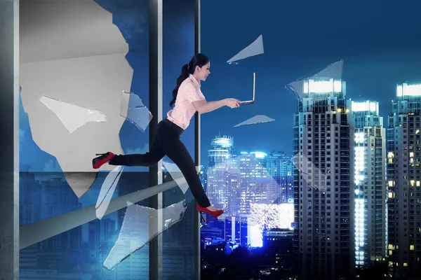Mulher com laptop saltar através da janela do escritório — Fotografia de Stock