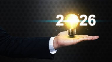 İş adamı 2026 'yı parlak bir ampulle gösteriyor. Mutlu yıllar konsepti ya da kutlama