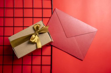 Altın kurdeleli kahverengi bir hediye kutusunun üst görüntüsü ve renkli bir arka planda kırmızı bir zarf. Model ya da kopyalama alanı. Yıldönümleri, kutlamalar, hediyeler veya sürprizler için dekorasyon kavramı