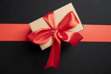 Renkli bir arka planda kırmızı kurdeleyle bağlanmış kahverengi bir hediye kutusunun üst görüntüsü. Model ya da kopyalama alanı. Tatiller, yıldönümleri, kutlamalar, hediyeler veya sürprizler için dekorasyon kavramı