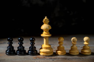 Beyaz satranç kralının, siyah ve beyaz satranç piyonları arasında duran karanlık bir arka plan görüntüsü. Liderlik veya yönetim kavramı