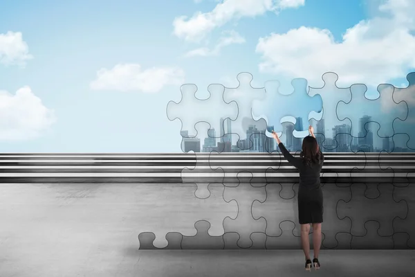 Business woman holding piece of puzzle trying to build a city — Stock Photo, Image