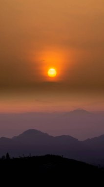 Altın ışık ve atmosferik bulutlarla dolu bir sıradağda canlı bir günbatımı sahnesi. Doğal arkaplan