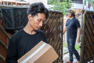 Endonezyalı güneydoğu Asyalı adam kask takan bir kuryeden karton bir paket alır. Teslimat servisi