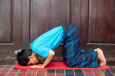 Endonezyalı Müslüman adam kırmızı bir hasırın üzerinde diz çöküyor ve başı yerde. Dua kavramı.