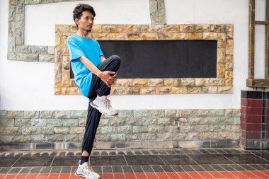 Mavi gömlekli ve siyah pantolonlu Endonezyalı yoga pozu veriyor. Egzersizden önce ısınıyor. Poz bölünmüş ve adam bacağını kaldırıyor. Odaklanma ve kararlılık kavramı. Adam duruşuna odaklanıyor.