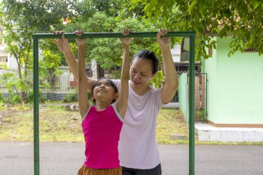 Mutlu Endonezyalı bir kadın genç bir kızın bir barda asılmasına yardım ediyor. Kız pembe bir gömlek giyiyor.