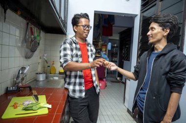 Mutfakta birlikte yemek hazırlarken iki Endonezyalı Güneydoğu Asyalı adam. Doğranmış malzemeler doğrama tahtasının üzerinde