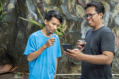 İki Endonezyalı güneydoğu Asyalı adam bir fincan kahve içerken rahatlamış ve arka planda bir cep telefonu ekranına bakıyorlardı. Kahve etkinliği