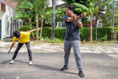 İki Endonezyalı güneydoğu Asyalı dışarıda egzersiz yapmadan önce ısınırken konuşuyor. Spor etkinliği