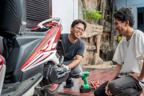Yeşil etkili ingiliz anahtarı olan Endonezyalı güneydoğu Asyalı tamirci, bir atölyede motosikleti inceledikten sonra parçanın müşterisiyle değiştirilmesini tartışıyor.