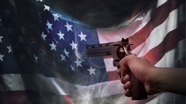 Amerikan bayrağı önünde tabanca tutan bir insan eli. Silahlı şiddet kavramı
